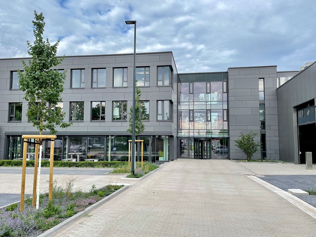 Firmenzentrale A. Jaeger Holding Blick von der Zufahrt aus auf die Eingangsfassade des Gebäudes mit Parkplätzen, Bäumen und Himmel
